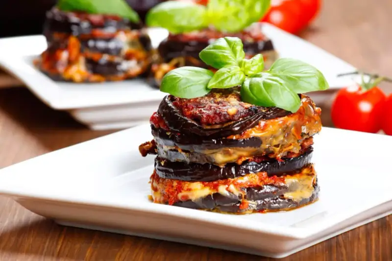Parmigiana di melanzane, un classico della cucina italiana, servita su un piatto bianco con basilico fresco.