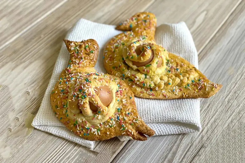 Due cuddure cu l'ova, dolci pasquali decorati con zuccherini colorati, riposano su un panno bianco.