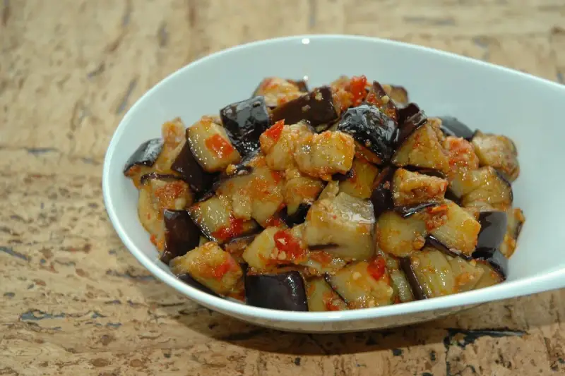Melanzane al microonde, tagliate a cubetti e condite con pomodoro e spezie, servite in una ciotola bianca.