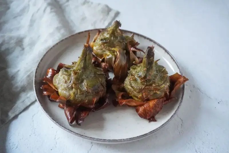 Tre carciofi alla giudia dorati e croccanti su un piatto, pronti per essere gustati.