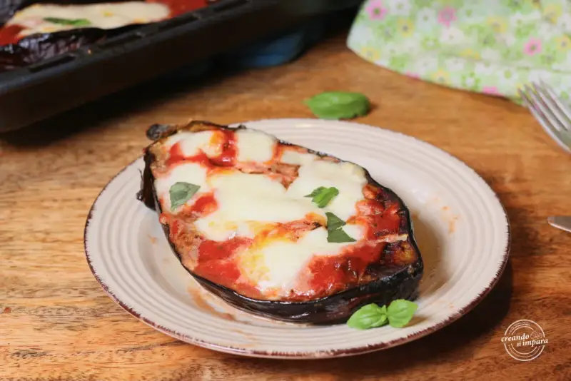 Melanzane alla pizzaiola appena sfornate, con mozzarella filante e basilico fresco su un piatto rustico.
