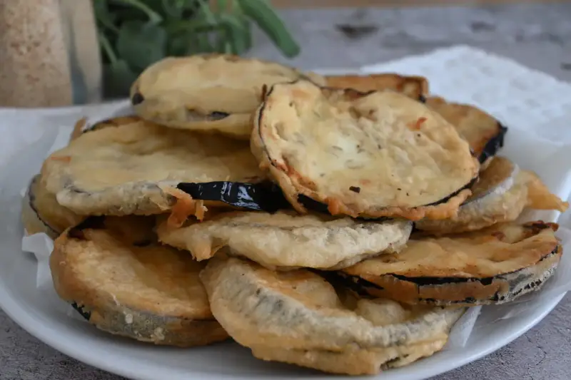 Piatto di melanzane fritte pastellate, dorate e croccanti, pronte per essere gustate.